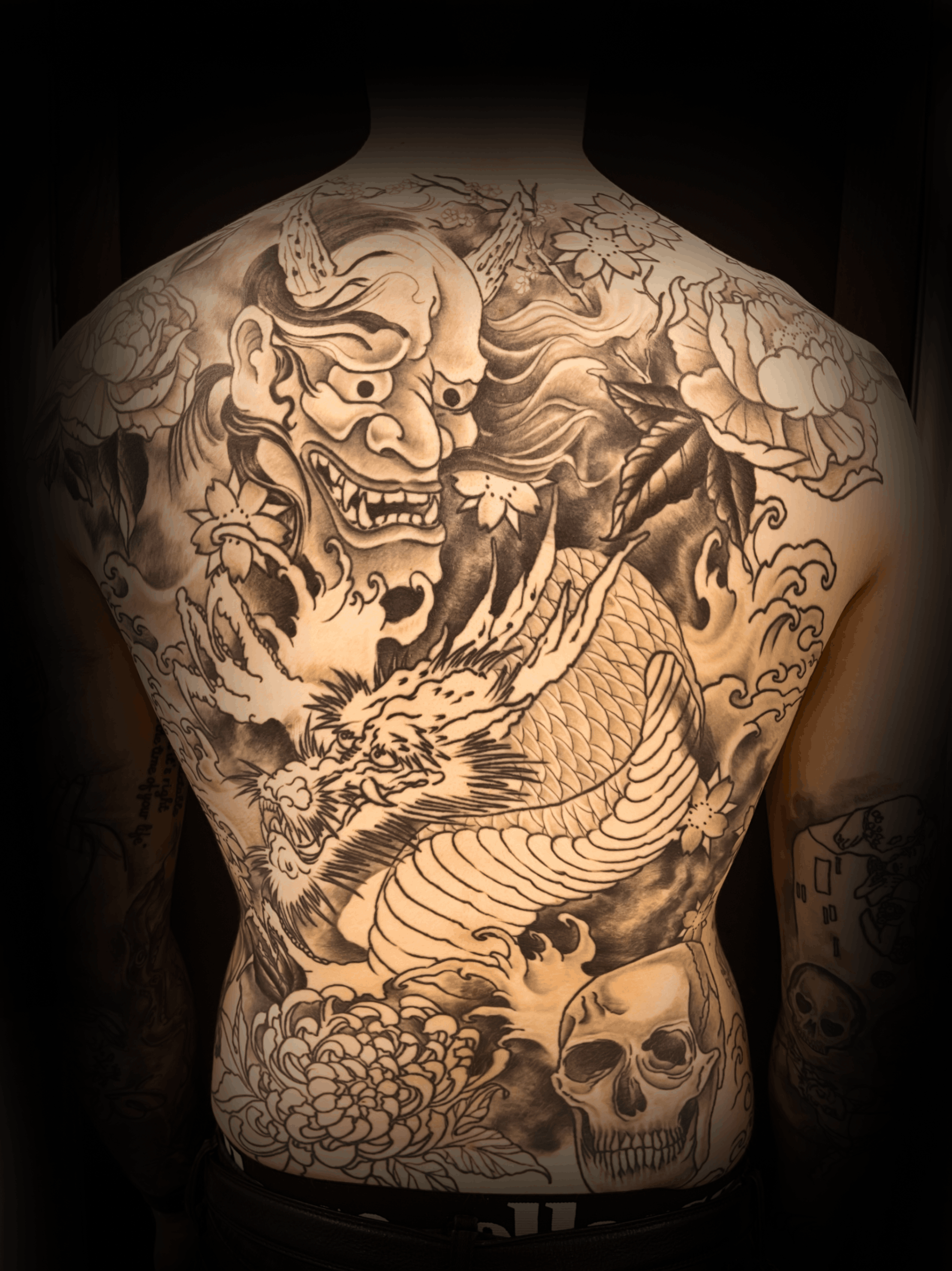 An image of a custom tattoo from Kevin Younger's Lucky Cat Tattoo Parlour: a design featuring traditional Japanese with a mask, skull, and dragon