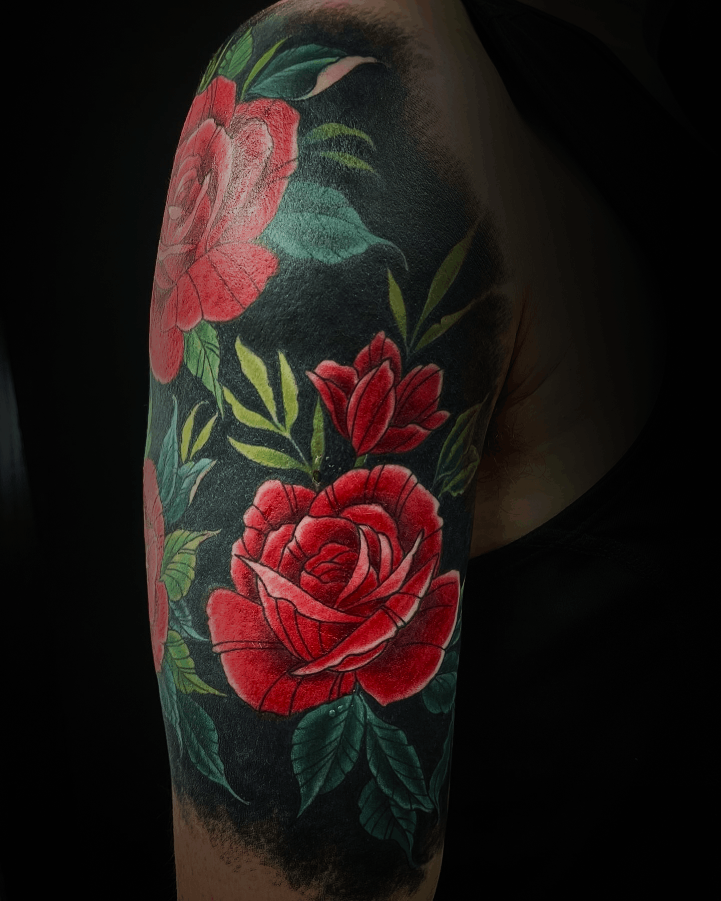 An image of a custom tattoo from Kevin Younger's Lucky Cat Tattoo Parlour: a design featuring a cluster of red roses with a dark background