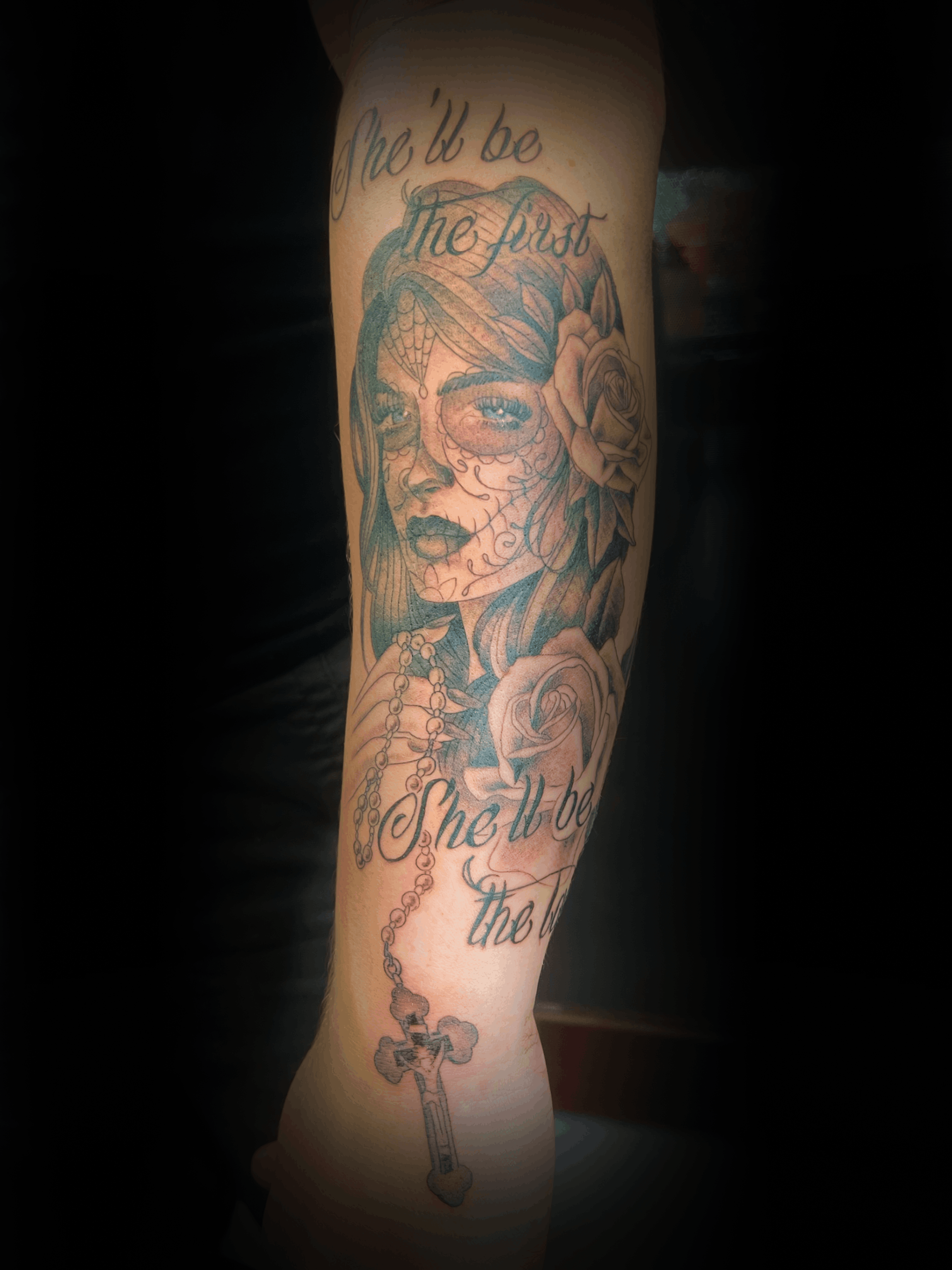 An image of a custom tattoo from Kevin Younger's Lucky Cat Tattoo Parlour: a design featuring a female portrait with script style text, a rose, and a cross
