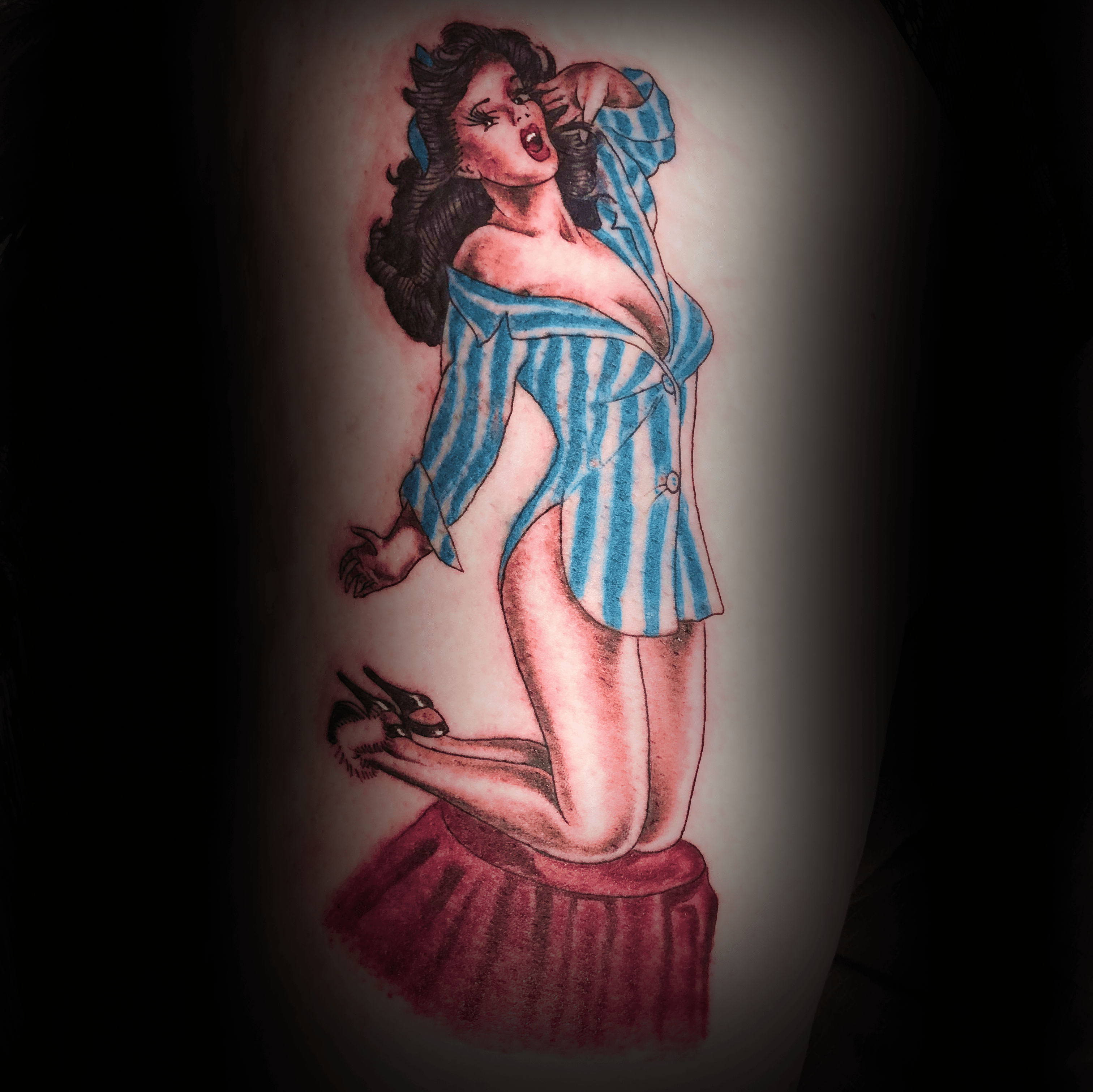 An image of a custom tattoo from Kevin Younger's Lucky Cat Tattoo Parlour: a design featuring a colourful retro style pin up girl kneeling on a velvet stool